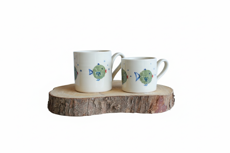Stable Door Pottery Two ceramic mugs with fish designs on a wooden coaster against a white background