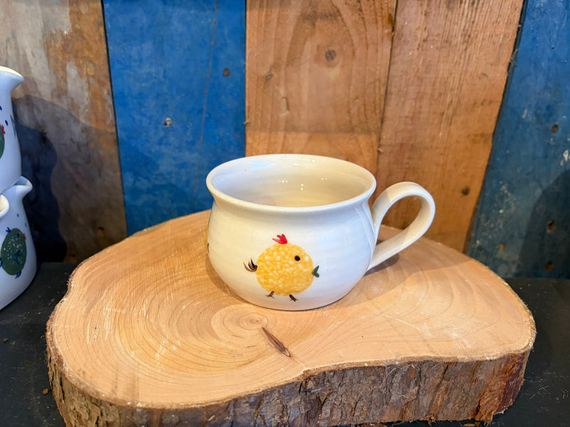 White mug with a yellow chick design on a wooden surface