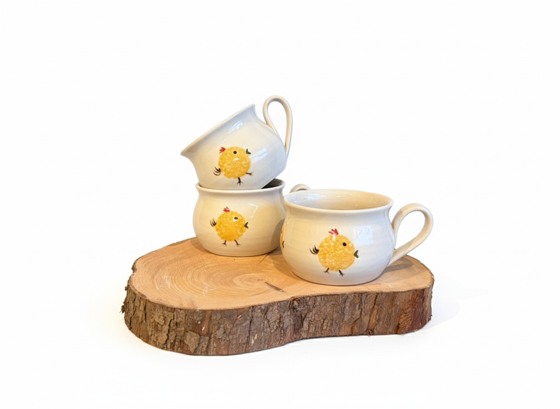 Set of ceramic cups with chick designs on a wooden stand against a white background