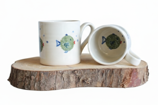 Two ceramic mugs with fish designs on a wooden surface